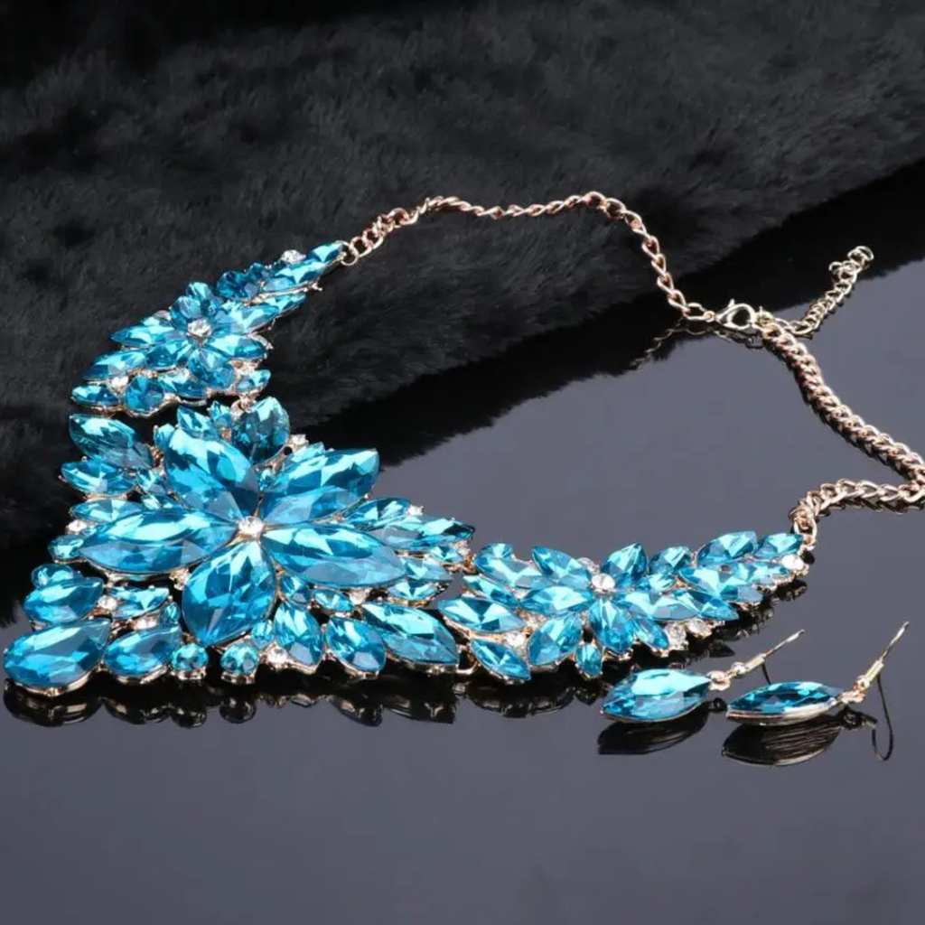Elegant blue crystal bridal jewelry set with floral statement necklace and matching earrings on gold chain, perfect for weddings and formal occasions