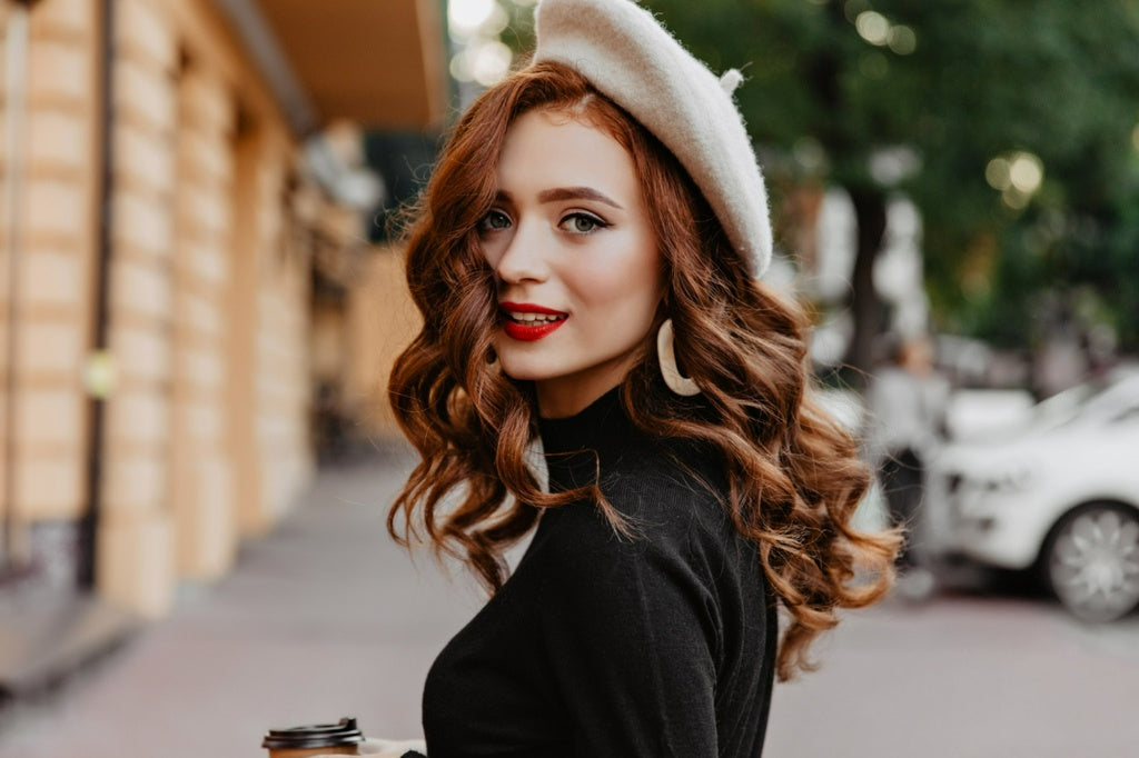 Fashionable woman wearing a cream-colored beret and black turtle neck with wavy red hair, representing Havenicstore's beauty and fashion collection.